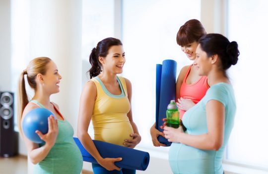 group of happy pregnant women talking in gym